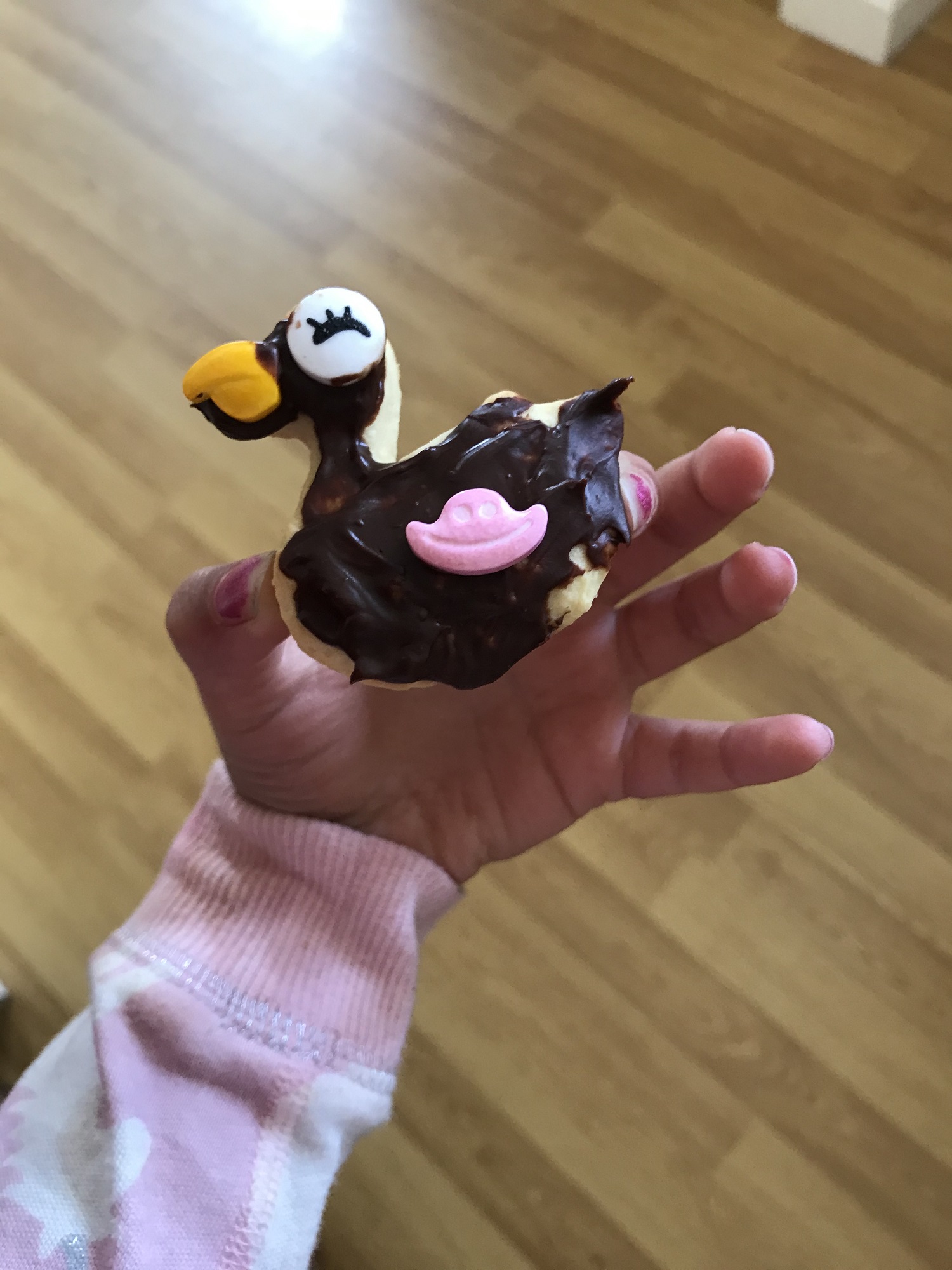 A duck-shaped biscuit is held by a small child. It has been decorated with a bright beak and white head